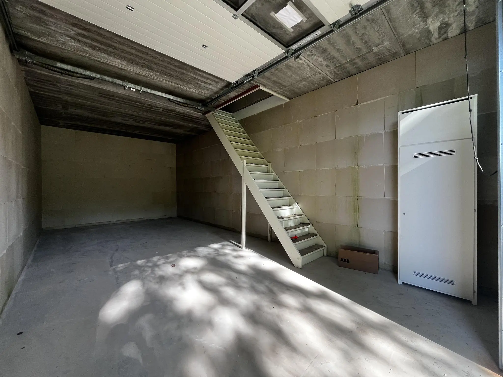 Lege betonnen garage of opslagruimte aan Broekdijk West 19-4 met witte trap en kast.